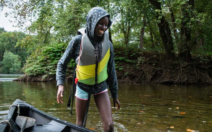 a student smiles as they walk through water beside a canoe on an outdoor trip